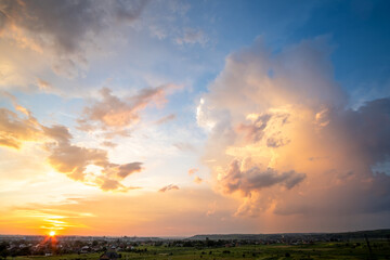 Dramatic sunset landscape of rural area with stormy puffy clouds lit by orange setting sun and blue sky.