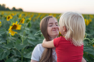 Portrait of mother and little son on field of sunflowers background. Young mother holds her son