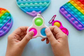 colorful trendy antistress sensory toy fidget push pop it and simple dimple in kid's hands on blue background