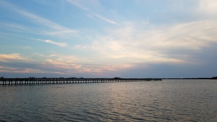 Pastel pink and blue clouds over a wooden fishing pier at sunset