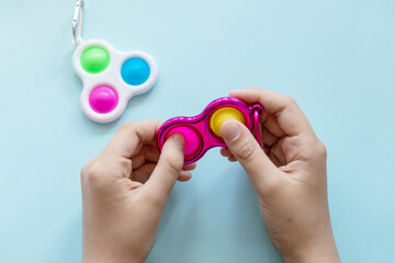 colorful trendy antistress sensory toy fidget push pop it and simple dimple in kid's hands on blue background