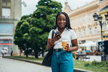 Cheerful african american woman using smartphone and drinking coffee takeaway