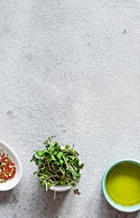 Fresh radish microgreens in a bowl with olive oil and pepper mix on a gray backgroundon a gray background. Healthy lifestyle concept, Vegan food. Growing sprouts. Salad dressing.