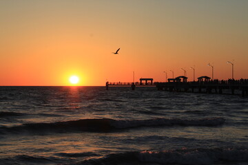 Fototapeta na wymiar Fishing pier at the beach with the sun on the horizon at sunset