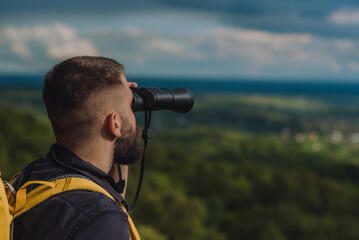 A hiker man using binoculars for orientation in the nature