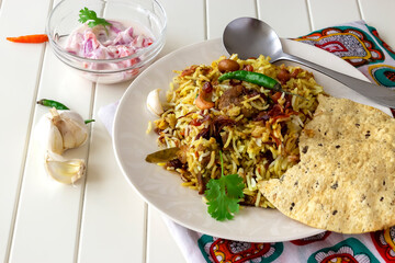 Traditional Indian mutton Biryani served with raita and crispy pappadam on white background. Selective focus. Authentic cuisine
