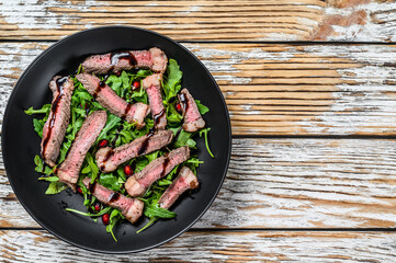 Sliced grilled beef steak with arugula leaves salad. White wooden background. Top view. Copy spac