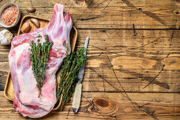 Whole Raw goat shoulder leg meat on a wooden tray. wooden background. Top view. Copy space