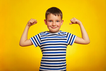 A child boy showing his hand biceps muscles strength on yellow background. Smart kid showing his...