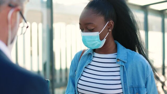 Close up of Caucasian man controller in mask on street checking health control scanning QR code of vaccination digital passport on smartphone app and measuring temperature of afro tourist