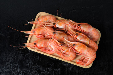 Boiled shrimps in a shell on a wooden bamboo plate on a black wooden surface.