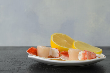 Boiled shrimp tails in a ceramic bowl with a raw scallop in the shell and lemon on a dark wooden background.