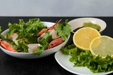 Natural raw scallop with boiled shrimp in the sink in a ceramic bowl with lettuce leaves and sauce on a dark background.