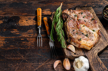 Roasted pork chop steak on a cutting board. Dark wooden background. Top view. Copy space