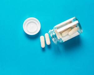 Naklejka premium white capsule pills from a glass jar. blue background. the concept of treatment and prevention of colds and virus.