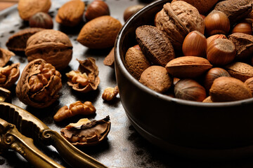 Almonds, walnuts and hazelnuts are sitting in a brown bowl and a nutcracker on a dark brown spotted plate.