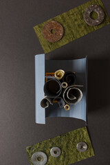composition with rolled paper in a yellow box on grey and rusty metallic washers on moss green paper - backgrounds 