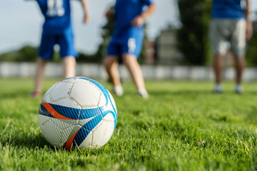 Close up on football ball during soccer training or game on the grass on field in sunny day with blurred players in background - sport concept copy space