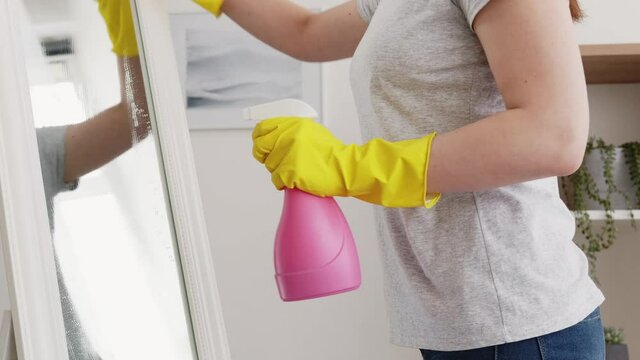 House chores. Housework service. Furniture hygiene. Unrecognizable woman in protective gloves cleaning mirror surface with spray and microfiber duster on light interior.
