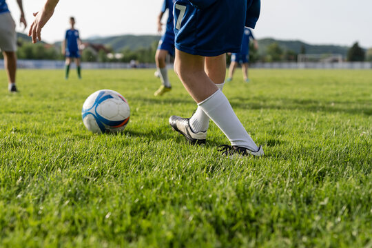 Close up on legs of unknown football soccer player caucasian boy child standing on the field in training or game by the ball kicking with unknown blurred players in background copy space