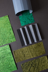 various shades of heavily textured green and pleated grey paper, on a dark background -...