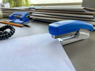 A large blue stapler for stapling paper lies next to the folders of documents on the working...