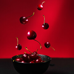fresh red juicy cherries falling to a little black bowl