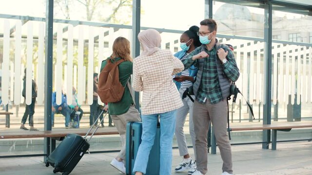 Mixed-race happy young different people meeting on street greeting with elbows during coronavirus pandemic ready for trip together. Male and female friends travelling with suitcases and backpacks