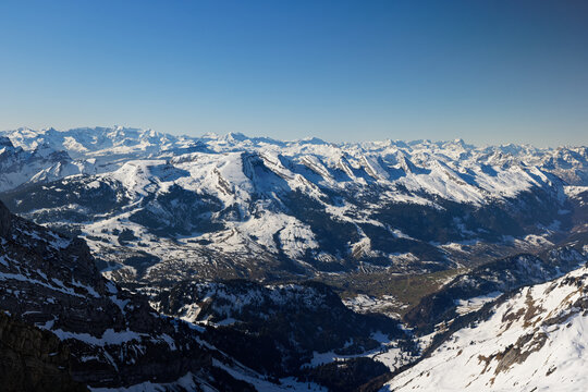 swiss mountain landscape in the snow photographed from bird's eye view, cloudless sky with extreme visibility, daytime, without people, in the background the seven churfirsten mountains