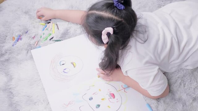 Top view of  kid lying on the floor doing painting by coloured pencils in living room with lots of happiness. Art activity at home