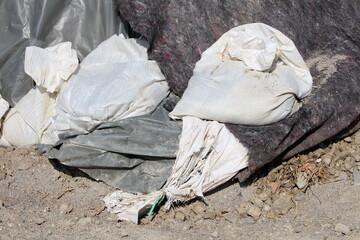 Bunch of new and old broken and ripped apart white sandbags holding thick dark nylon protection and geotextile fabric covering temporary flood protection wall made of box barriers and sandbags used to