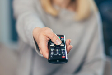 Woman holding a remote control from the TV switches channels