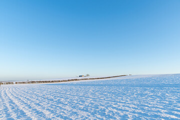 A sunny snowy farm on a hill in rural countryside during winter