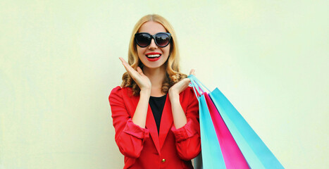 Portrait of happy smiling young woman with shopping bags wearing a red business blazer on a background