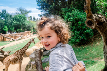 Happy girl on her first visit to a zoo visiting giraffes - obrazy, fototapety, plakaty