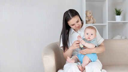 Caring for the concept of a newborn. A young mother sitting on the sofa with her baby on her lap, looks at her child with love and care. the concept of family and motherhood is a happy smiling mother