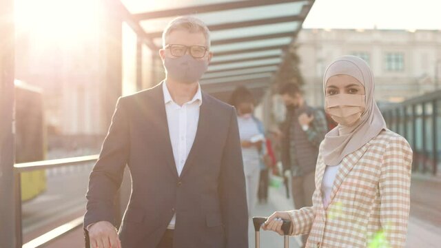 Portrait of happy multi-ethnic people wearing protection masks standing in town outside and looking at camera at bus stop. Business partners trip. Businessman and business lady at bus station