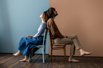 Guy and girl sit back to back on a chair. Background is divided into two halves.