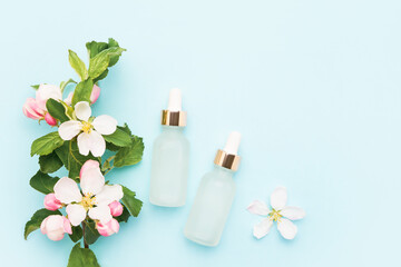 Obraz na płótnie Canvas Glass dropper bottles for medical and cosmetic use and apple tree blossom flowers on a light blue background. SPA concept