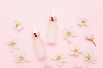 Obraz na płótnie Canvas Glass dropper bottles for medical and cosmetic use and apple tree blossom flowers on a pink background. SPA concept
