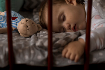 Cute cheerful little chubby baby girl sleeping sweetly in grey baby crib during lunch rest time in...