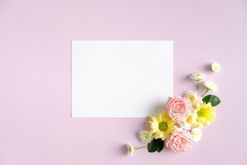 Blank paper card and flowers arrangement on pink background. Birthday or Mothers Day greeting card mockup.