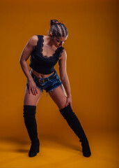 Trendy female model posing in studio with high black boots, shorts jeans and a black shirt