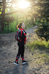 Woman in a tracksuit with camping bag in the forest at sunset.