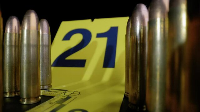 SLIDER SHOT PULLING BACK AWAY FROM AN EVIDENCE MARKER SURROUNDED BY RIFLE BULLETS.  4K, WIDE ANGLE, MACRO.  NO PEOPLE.