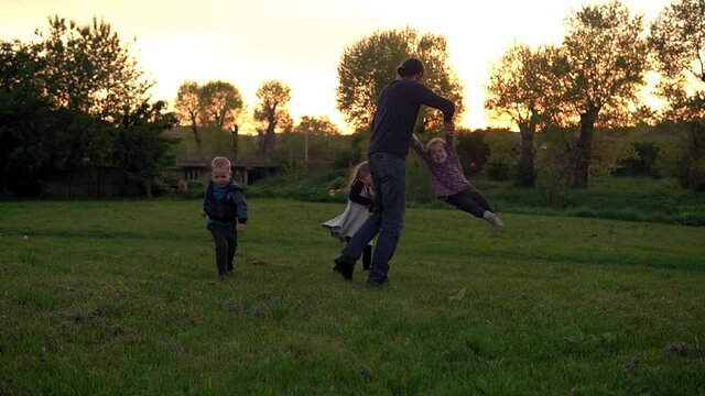 people in the park. happy family silhouette at sunset. dad swinging baby by hte hands have spend time. parents and fun children walking outdoors in open air. Fathers day, childhood, parenthood concept