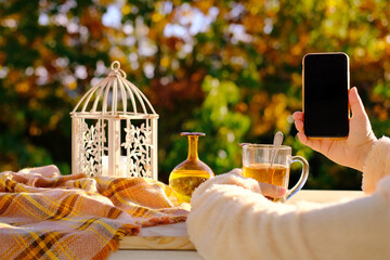 on the table in the garden tea in a glass mug, a candle is burning, a woman is holding a smartphone with a blank black screen, the concept of an outdoor tea party, good weather, a cozy mood