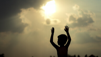 Fototapeta na wymiar Little boy raising hands over sunset sky, enjoying life and nature. Happy Kid on summer field looking on sun. Silhouette of male child in sunlight rays. Fresh air, environment concept.