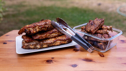 A plate and a glass bowl with grilled pork ribs on a wooden table.