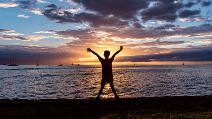 Silhouette of a little girl standing with hands in the air against scenic sunset, Lahaina bay, Maui, Hawaii